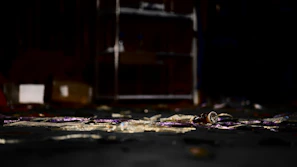 Dimly lit crime scene with scattered evidence and a shadowy figure in the background