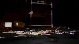 Dimly lit crime scene with scattered evidence and a shadowy figure in the background