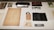 A collection of vintage items is displayed on a surface. Items include a harmonica, a pair of round spectacles, a worn book or document, an old identification card, photographs, and a leather case. The items are meticulously arranged and labeled, suggesting a historical or personal significance.