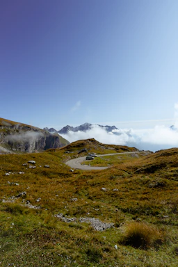 A serene mountain road winding through lush green hills with a sleek taxi parked by the roadside under a clear blue sky.