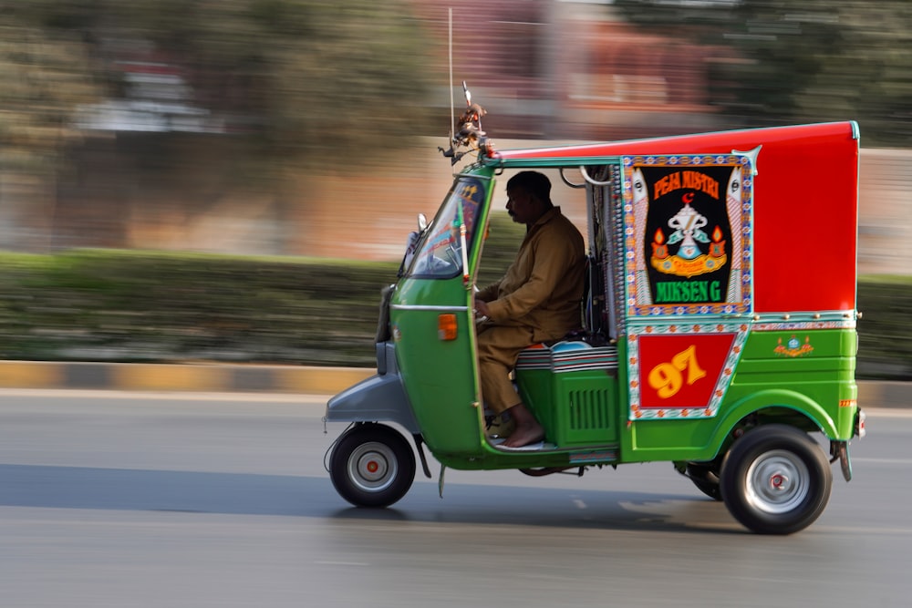 a man driving a green and red truck down a street