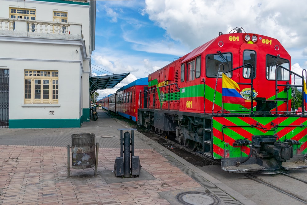a red and green train parked next to a white building