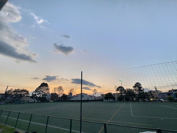 Wide shot of a sports field surrounded by durable wire mesh fencing with evening lighting.