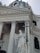A grand architectural structure featuring a classical building with tall columns and intricate moldings. A prominent statue of an angel holding a large cross stands in front, with a large dome and smaller statues on top. The facade includes Latin inscriptions.