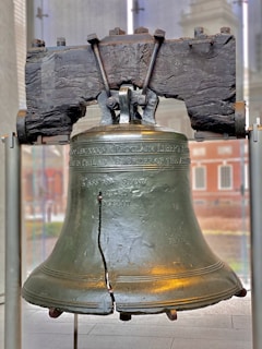 A vintage Liberty Bell with its iconic crack, resting on a wooden stand.