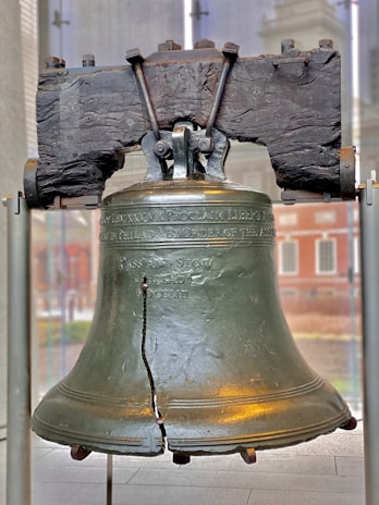 A vintage Liberty Bell with its iconic crack, resting on a wooden stand.
