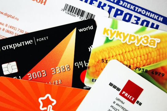 A collection of colorful credit or membership cards overlapping each other, featuring various designs including a corn image, geometric shapes, and text in different languages.