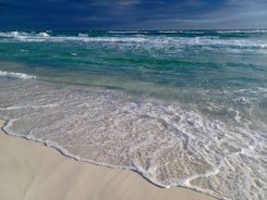 Turquoise waves gently lapping against a white sandy beach under a clear blue sky.