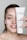 A person with light skin is smiling and holding up a tube of Janssen Cosmetics Thermo Peel Mask Cranberry next to their face. They have applied some of the mask to their cheek, and their nails have a delicate design.
