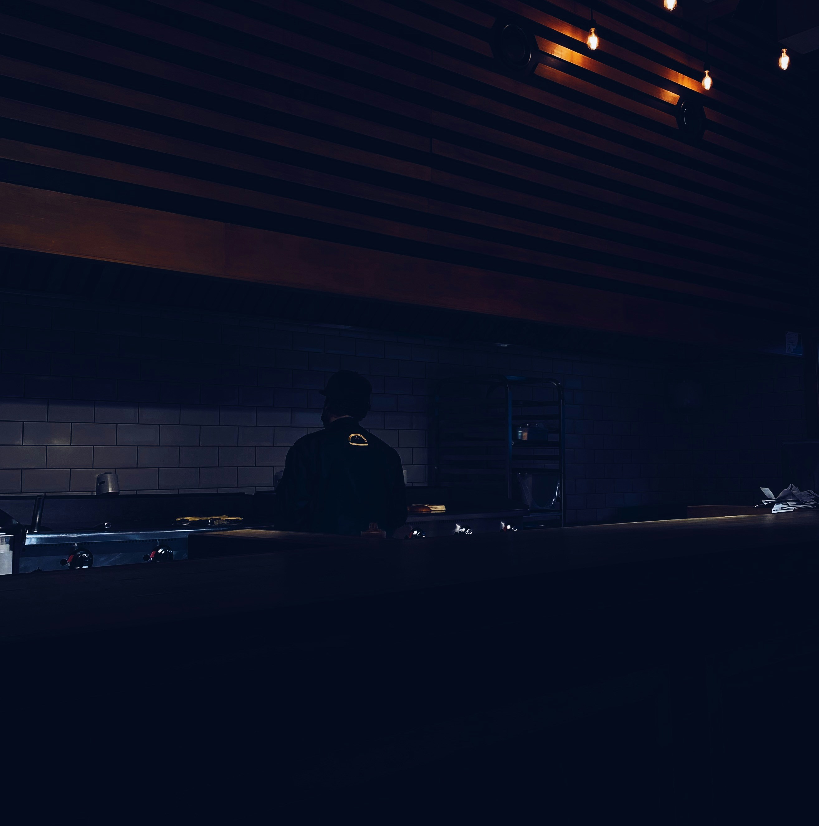 Chef in dark kitchen with dramatic pendant light illuminating a single dish on white porcelain