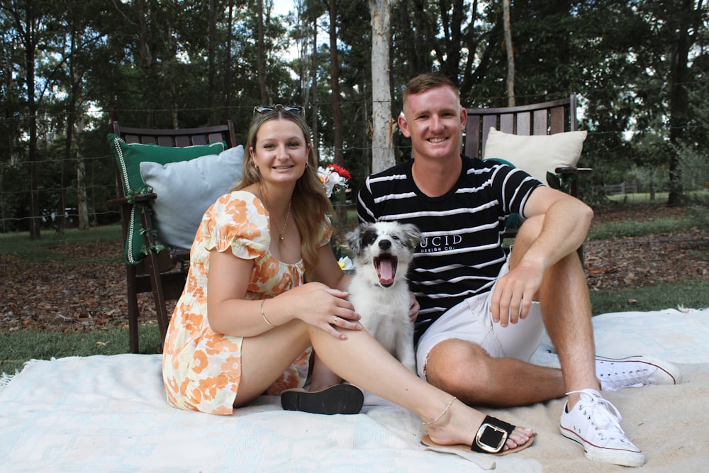 a man and a woman sitting on a blanket with a dog