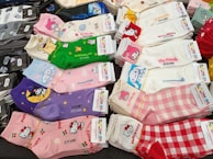 A variety of colorful socks featuring popular cartoon characters are neatly arranged in stacks. These socks include a variety of designs, each showcasing different characters and themes. The designs display playful and cute motifs with vibrant patterns.