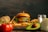 A juicy hamburger with lettuce, tomato, and cheese sits on a wooden board surrounded by crispy French fries. Fresh ingredients such as a whole avocado, sliced onion, a potato, and ripe tomatoes accompany the scene. A pair of salt and pepper shakers is positioned on the right side.