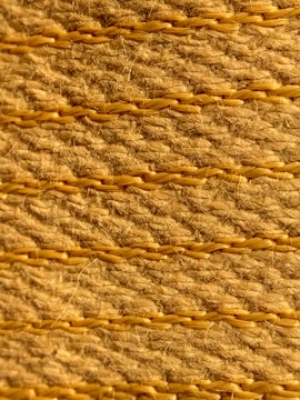 A close-up view of a textured woven surface featuring horizontal rows of tan and light brown fibers intertwined with visible strands. The fibers appear coarse, with occasional hair-like strands protruding, highlighting the natural texture and craftsmanship.