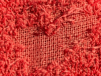 A close-up view of a red, frayed fabric, revealing its woven structure with visible threads and fibers.