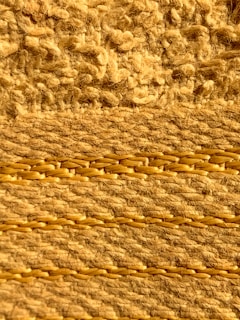 A close-up view of a woven fabric texture, displaying a detailed pattern of thick, braided yarns intertwined with loops and knots. The texture appears coarse and rustic, revealing the intricate craftsmanship involved in its creation.