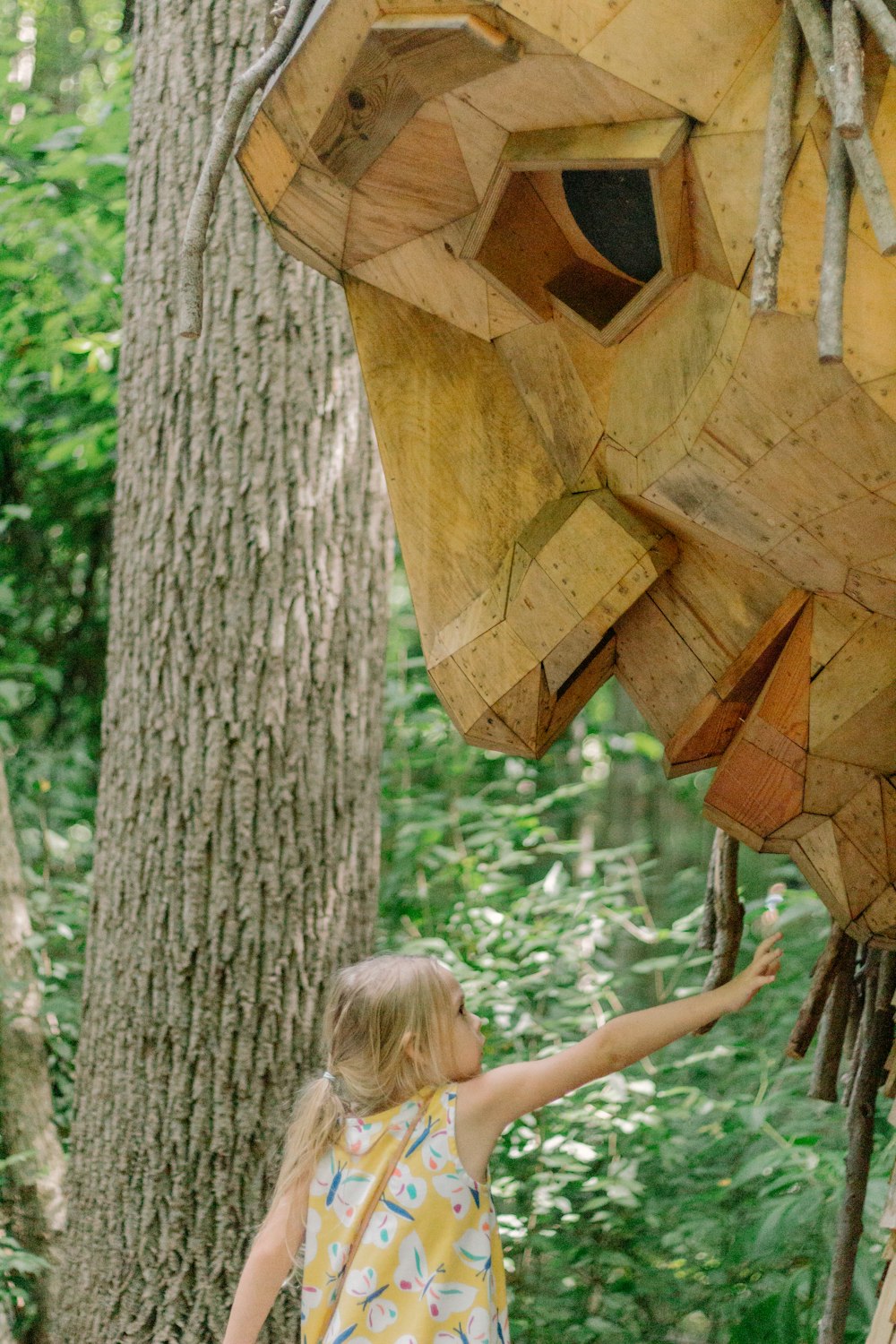 a little girl reaching up to a wooden sculpture