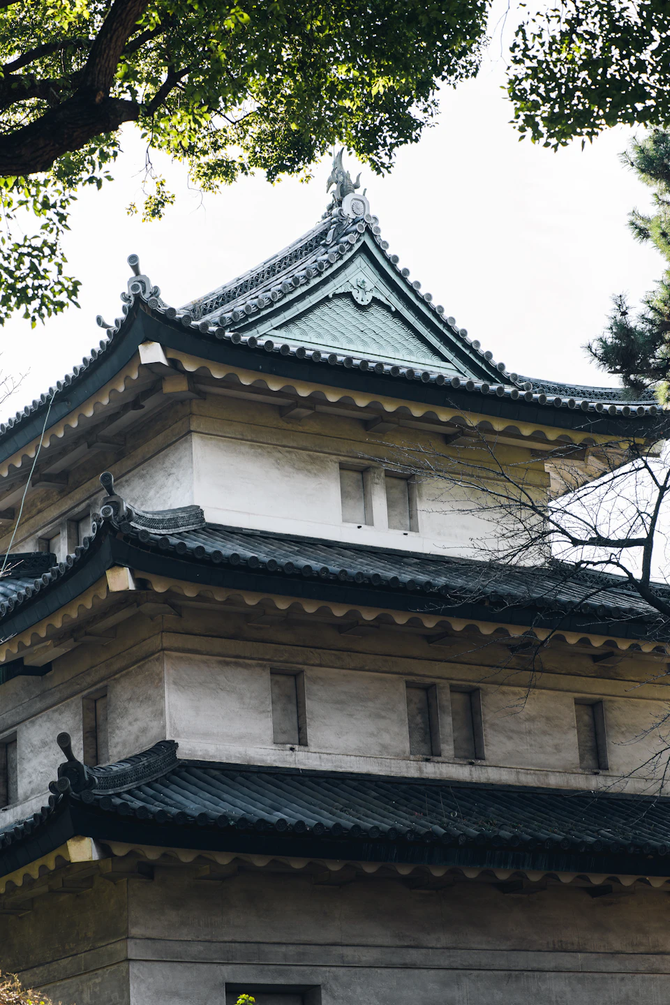 The image shows a traditional Japanese temple with three levels, each adorned with a green roof and white walls. The temple is situated amidst nature, surrounded by trees that provide a serene backdrop to its architectural beauty. The perspective of the photo is from below, looking up at the temple's impressive height and intricate details.

The image does not contain any discernible text or countable objects, but it captures the essence of traditional Japanese architecture in a peaceful setting.