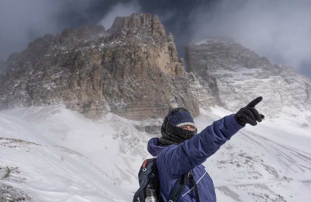 um homem em uma jaqueta azul apontando para uma montanha