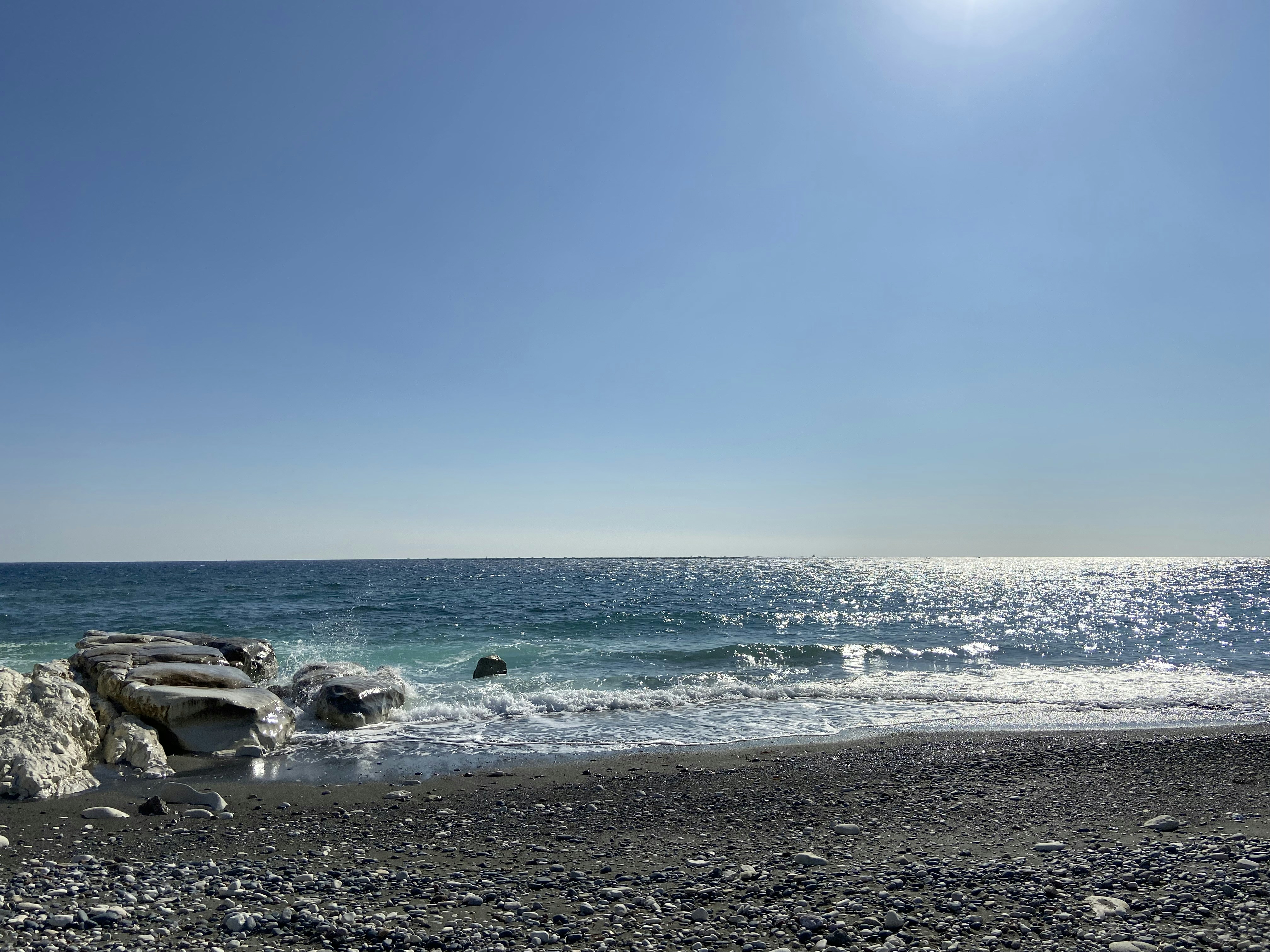 the sun shines brightly over the ocean on a rocky beach