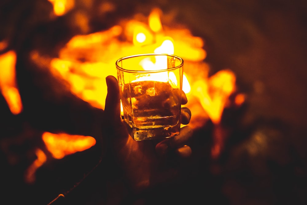 a person holding a glass in front of a fire