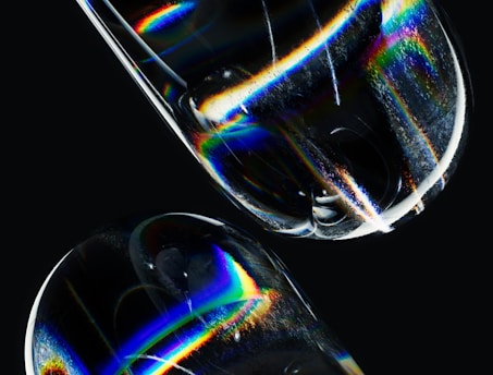 Abstract image featuring prismatic light refractions on a smooth, transparent surface with rainbow-like colors. The dark background contrasts with the bright spectral bands, enhancing the visual impact.