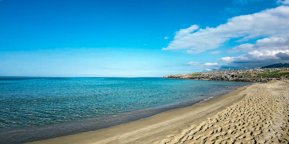 a sandy beach next to the ocean under a blue sky