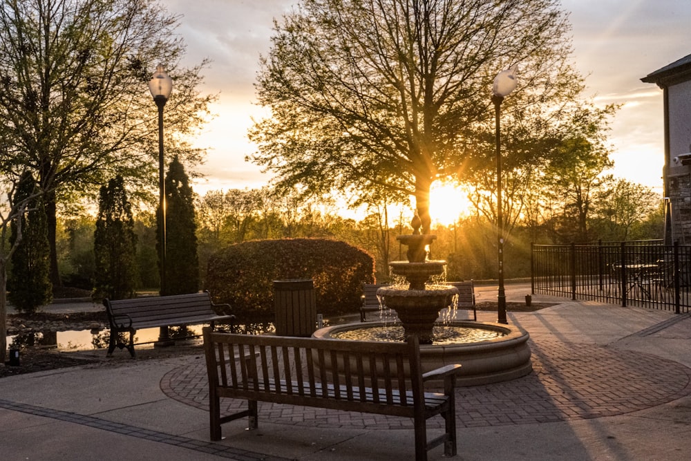 a park with benches and a fountain at sunset