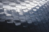 Interlocking dark metallic panels create a geometric pattern with subtle reflections of light across their surfaces, giving a modern and sleek appearance.