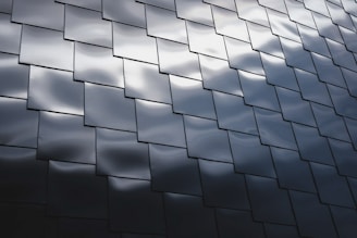 Interlocking dark metallic panels create a geometric pattern with subtle reflections of light across their surfaces, giving a modern and sleek appearance.