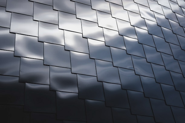 Interlocking dark metallic panels create a geometric pattern with subtle reflections of light across their surfaces, giving a modern and sleek appearance.