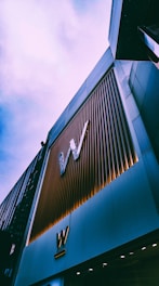 A tall building with a modern facade, featuring vertical metal slats and large 'W' logos. The architectural style appears contemporary, with a sleek and polished look. The sky above is overcast, contributing to a subdued atmosphere.