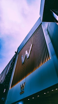 A tall building with a modern facade, featuring vertical metal slats and large 'W' logos. The architectural style appears contemporary, with a sleek and polished look. The sky above is overcast, contributing to a subdued atmosphere.