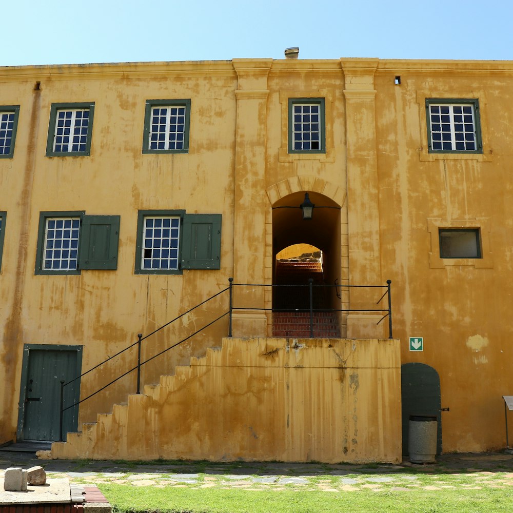 a yellow building with green shutters and a staircase