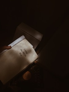 A person holds two books, one titled 'Living the 80/20 Way' and another partially visible book titled 'The Culture Code'. The scene is dimly lit, with the light casting shadows across the books.