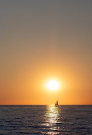 A serene sailboat gliding on calm blue waters under a golden sunset.