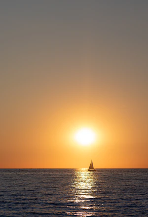 A serene sailboat gliding on calm blue waters under a golden sunset.
