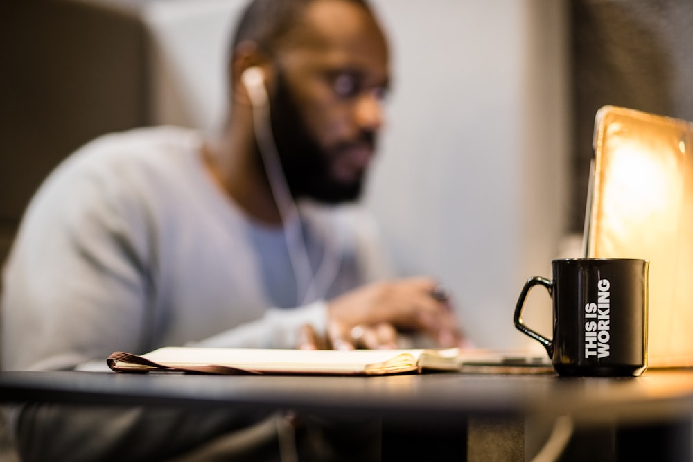 a man sitting at a table with a laptop and a coffee mug