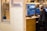 A person sits at a wooden desk working on video editing software seen on dual monitors. They wear headphones and appear focused. The workspace is modern, featuring light brown wooden panels and shelves with decorative items. A mug and keyboard are placed on the desk.