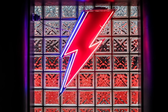 A bright yellow electric bolt overlay on a blue-toned photo of an electrician installing wiring.