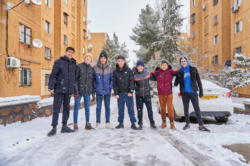 A group of volunteers handing out winter hats and gloves to homeless youth on a snowy street.
