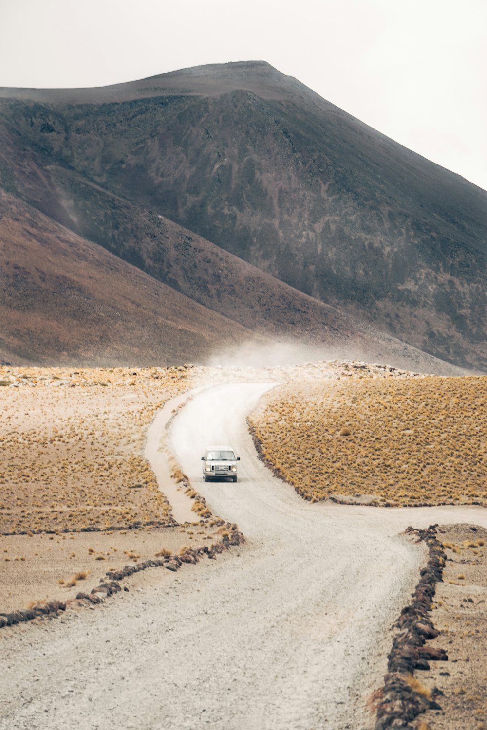 a car driving down a dirt road in front of a mountain