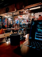A vibrant coffee place with young people working on laptops, featuring large windows and artistic decorations.