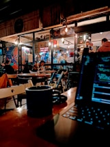 A cozy coffee place with young people working on laptops, featuring big windows and artistic decorations.