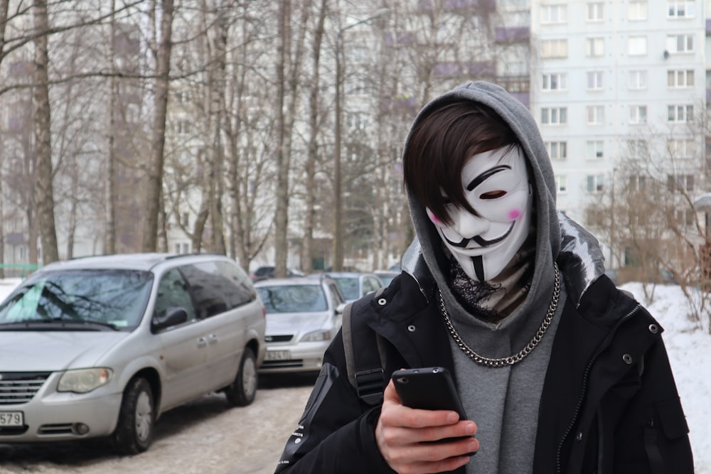 eine Person, die eine Maske trägt und ein Mobiltelefon hält