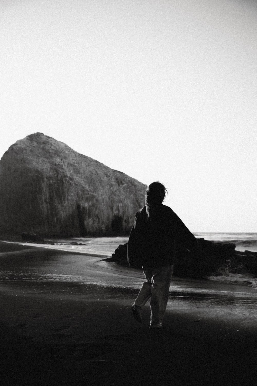 a black and white photo of a person walking on a beach