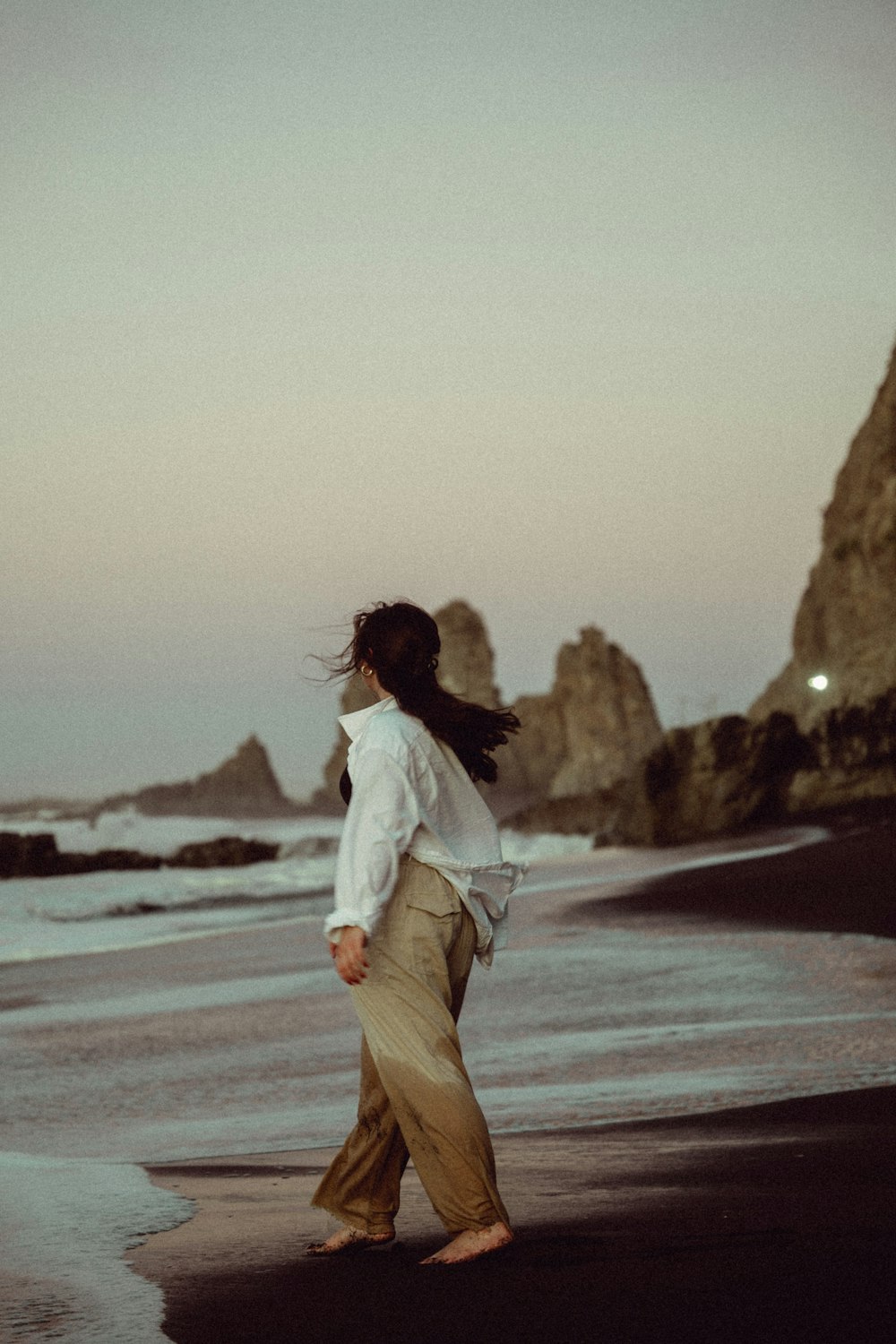 a woman walking along a beach next to the ocean