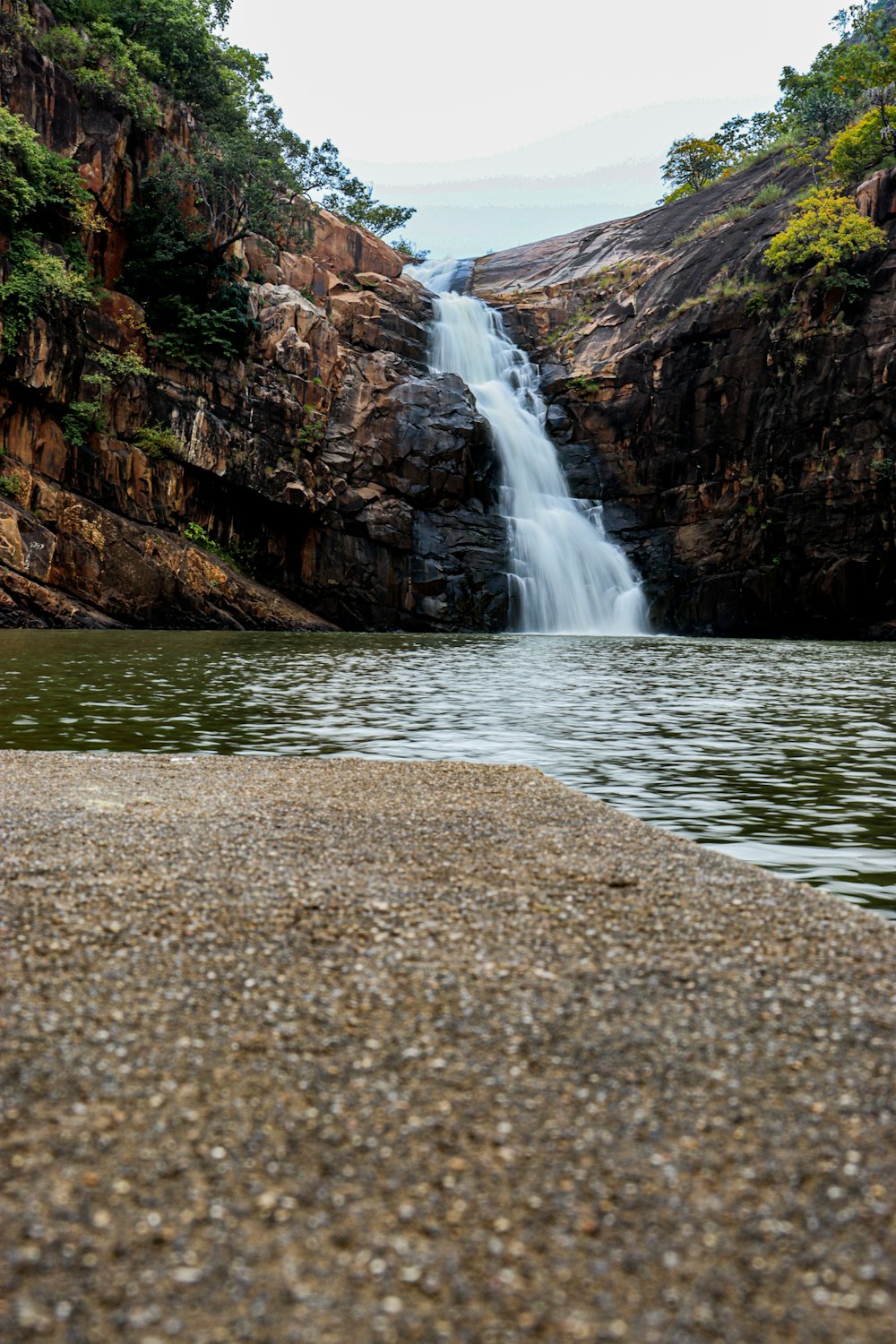 a view of a waterfall from the shore of a lake