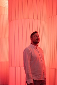 A person stands in a space illuminated by a vibrant red light, surrounded by large vertical columns with ribbed patterns. The lighting creates a warm and immersive atmosphere.
