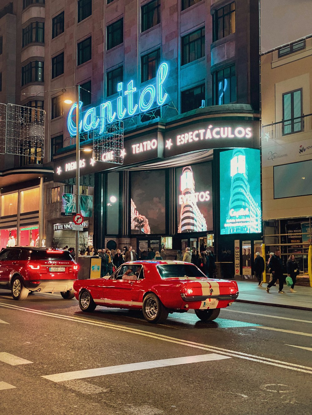 a red car driving down a street next to a tall building